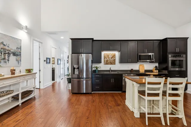 a kitchen with stainless steel appliances a stove a sink a refrigerator white cabinets and wooden floor