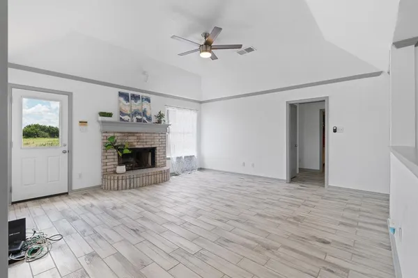 a view of an empty room with wooden floor a fireplace and a window