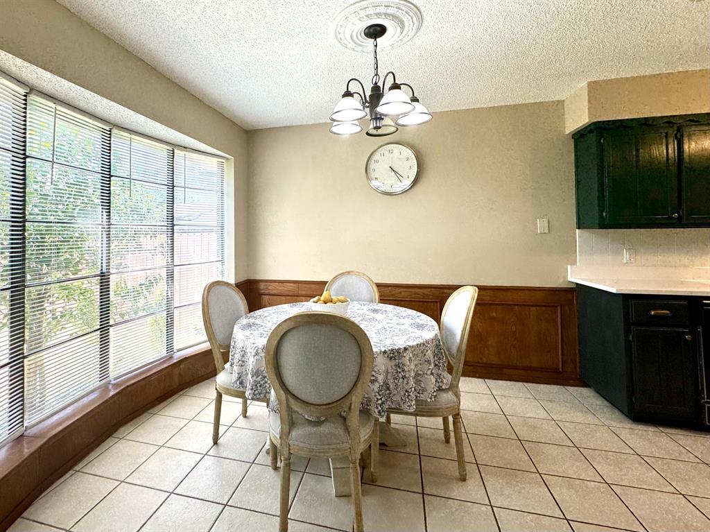 113 Northeast Timber Ridge Drive Burleson, TX 76028 - Photo 11 of 36 Bay window dining area featuring tile flooring, wood paneling, a ceiling medallion with a chandelier, and a built-in counter with cabinetry and a white subway tile backsplash