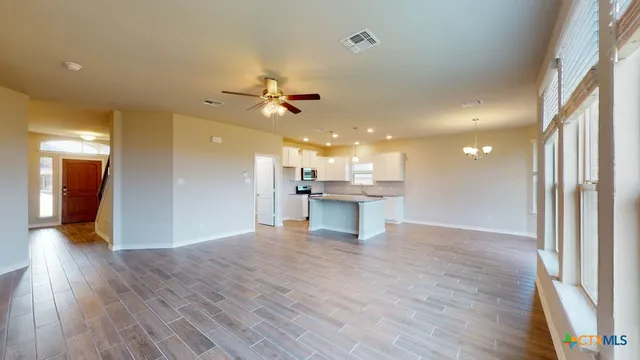 a view of an empty room with wooden floor and a kitchen