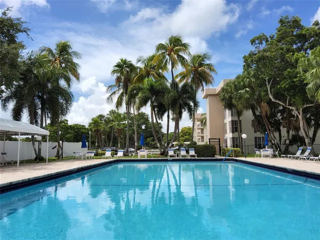 a view of a swimming pool with a lawn chairs under palm trees