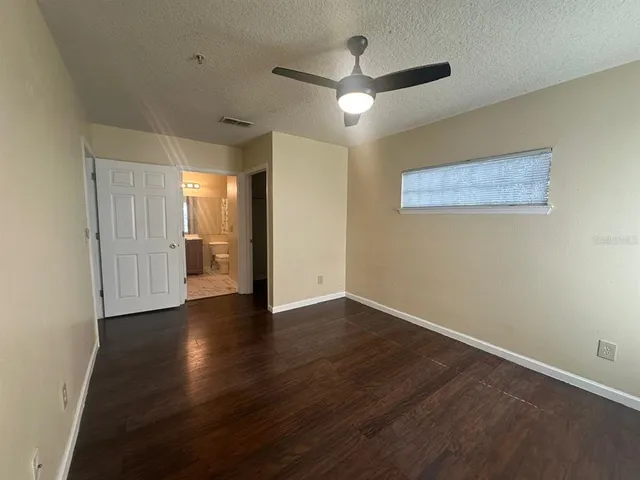 a view of an empty room with wooden floor and a ceiling fan