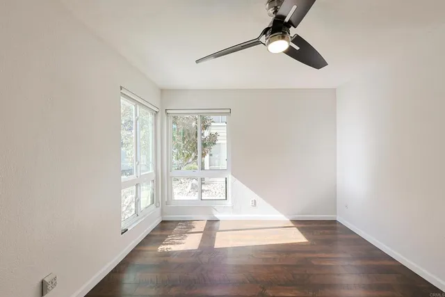 an empty room with wooden floor fan and windows