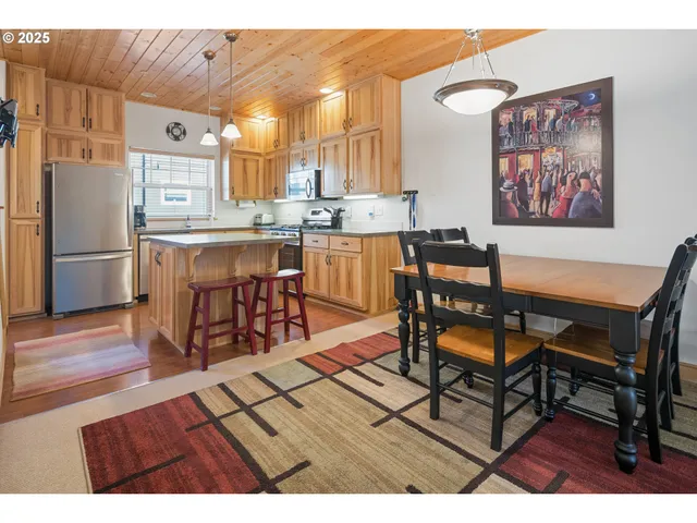 a open kitchen with stainless steel appliances kitchen island granite countertop a table chairs and a refrigerator