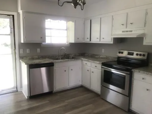 a kitchen with granite countertop white cabinets stainless steel appliances and a window