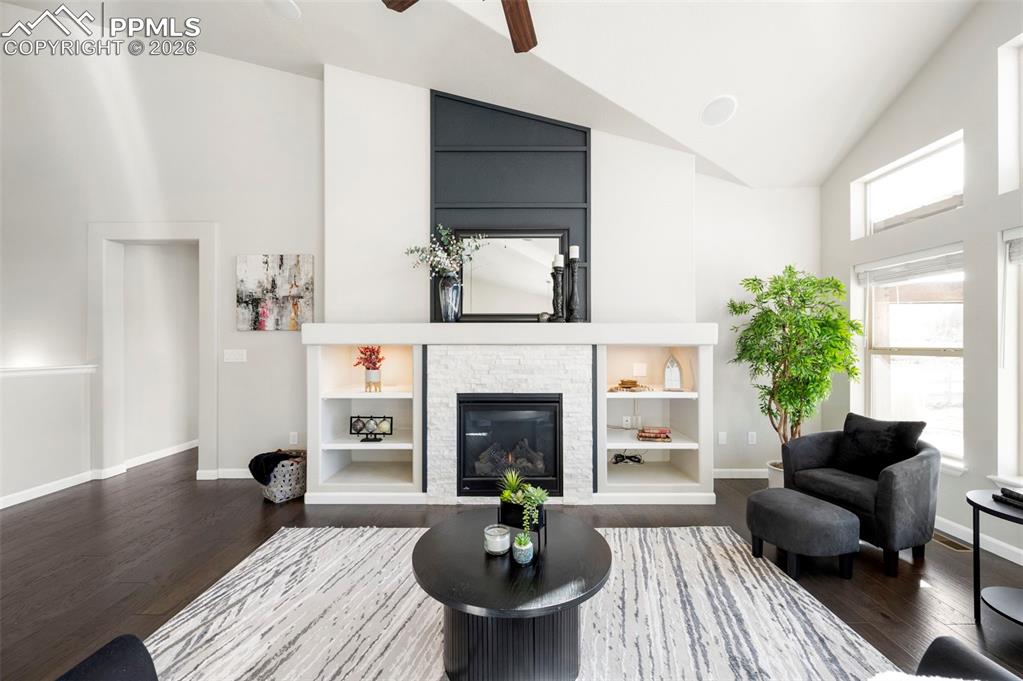 1073 Native Dancer Terrace Colorado Springs, CO 80921 - Photo 12 of 48 Living room with vaulted ceiling, dark wood-type flooring, built in shelves, a fireplace, and a ceiling fan