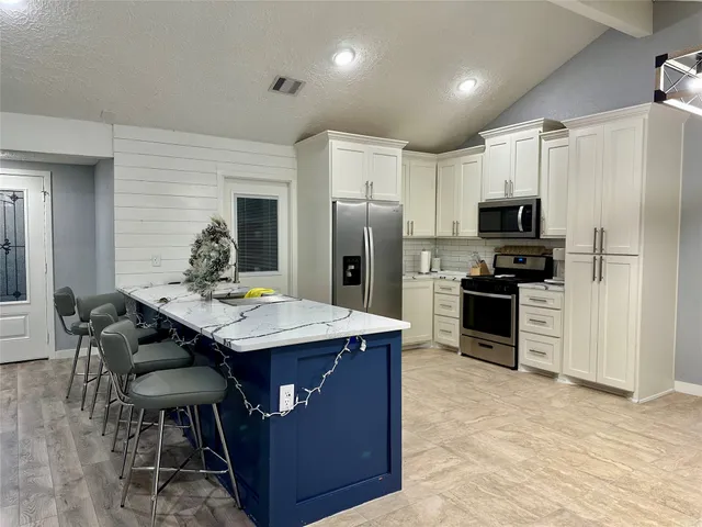 a kitchen with stainless steel appliances kitchen island granite countertop a table chairs refrigerator and microwave