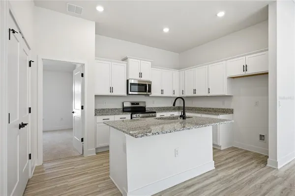 a kitchen with stainless steel appliances granite countertop a sink a stove a refrigerator and white cabinets