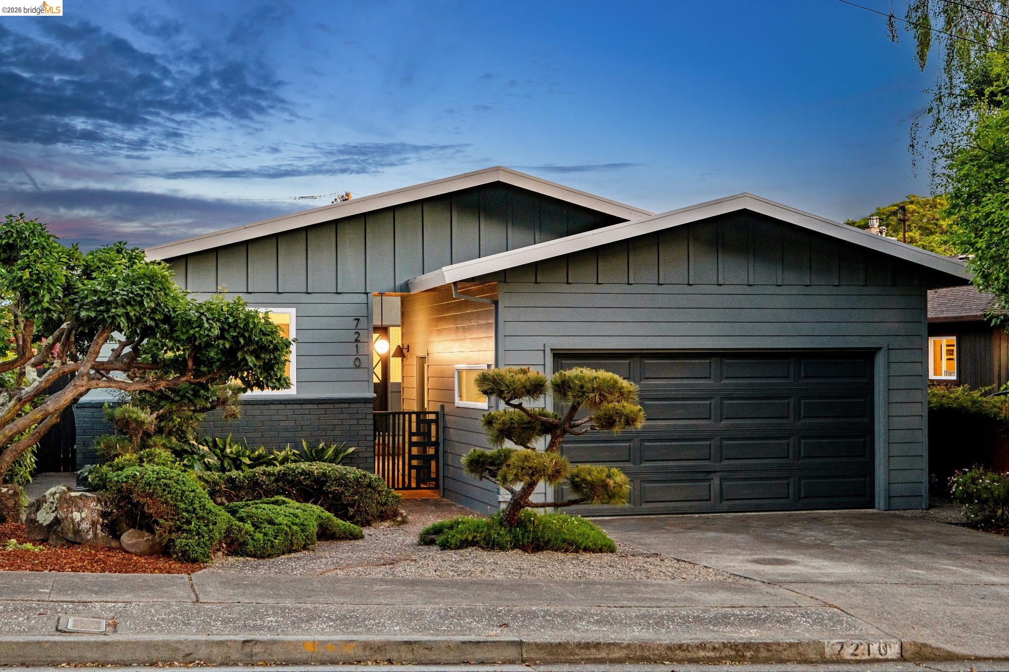 7210 Mound Street El Cerrito, CA 94530 - Photo 1 of 1 Ranch-style house with a garage, concrete driveway, and board and batten siding. Digitally altered to remove power line.