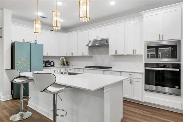 a kitchen with stainless steel appliances granite countertop a stove top oven a refrigerator a sink and a dining table with wooden floor