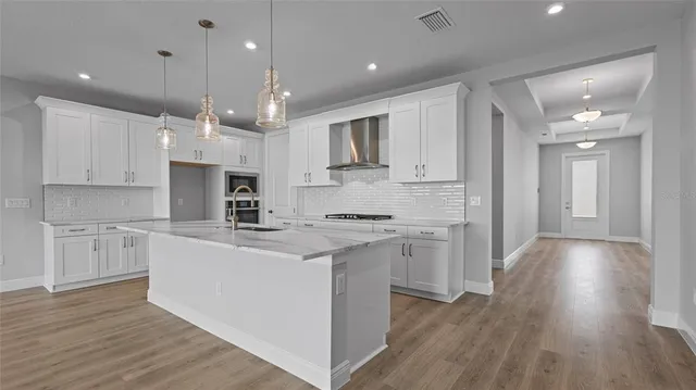 a kitchen with stainless steel appliances granite countertop a sink a stove a refrigerator and white cabinets with wooden floor