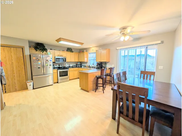 a kitchen with stainless steel appliances kitchen island granite countertop a stove a refrigerator a dining table and chairs with wooden floor