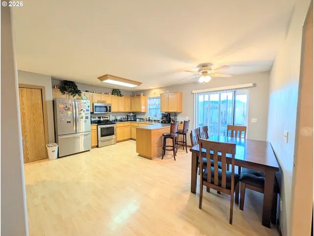 a kitchen with stainless steel appliances kitchen island granite countertop a refrigerator a stove a dining table and chairs with wooden floor