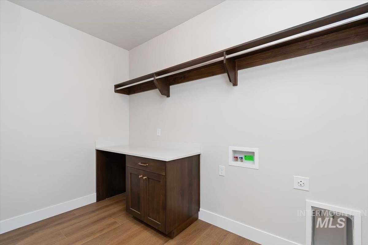 3321 Helios Street Caldwell, ID 83607 - Photo 30 of 35 Laundry area featuring wood-finish flooring, a built-in dark wood cabinetry with a light-colored countertop, and an integrated stainless steel utility sink