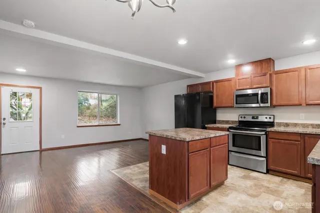 a kitchen with stainless steel appliances granite countertop a stove top oven a sink dishwasher and a refrigerator with wooden floor