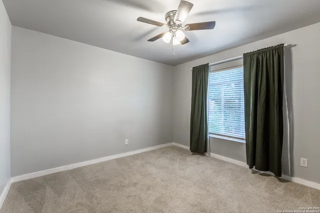 an empty room with chandelier fan and windows