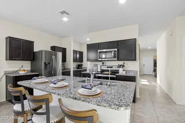 a kitchen with stainless steel appliances granite countertop a sink a stove a refrigerator cabinets and chairs