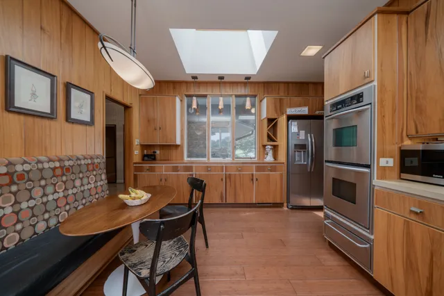 a kitchen with stainless steel appliances kitchen island granite countertop a table chairs in it and a window
