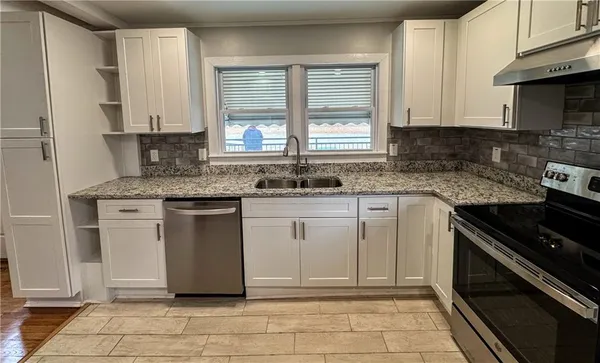 a white kitchen with granite countertop a stove sink and cabinets