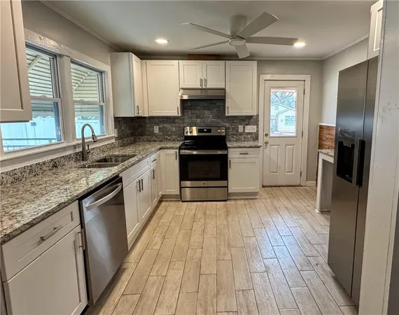 a kitchen with granite countertop wooden floors stainless steel appliances a sink and a window