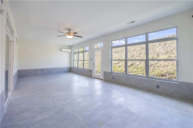 an empty room with chandelier fan and windows