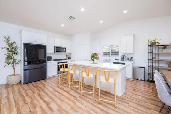 a kitchen with stainless steel appliances kitchen island granite countertop a refrigerator a stove top oven a sink dishwasher and white cabinets with wooden floor