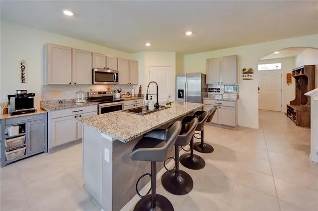 a kitchen with stainless steel appliances granite countertop a stove top oven a refrigerator a sink and a dining table with white cabinets