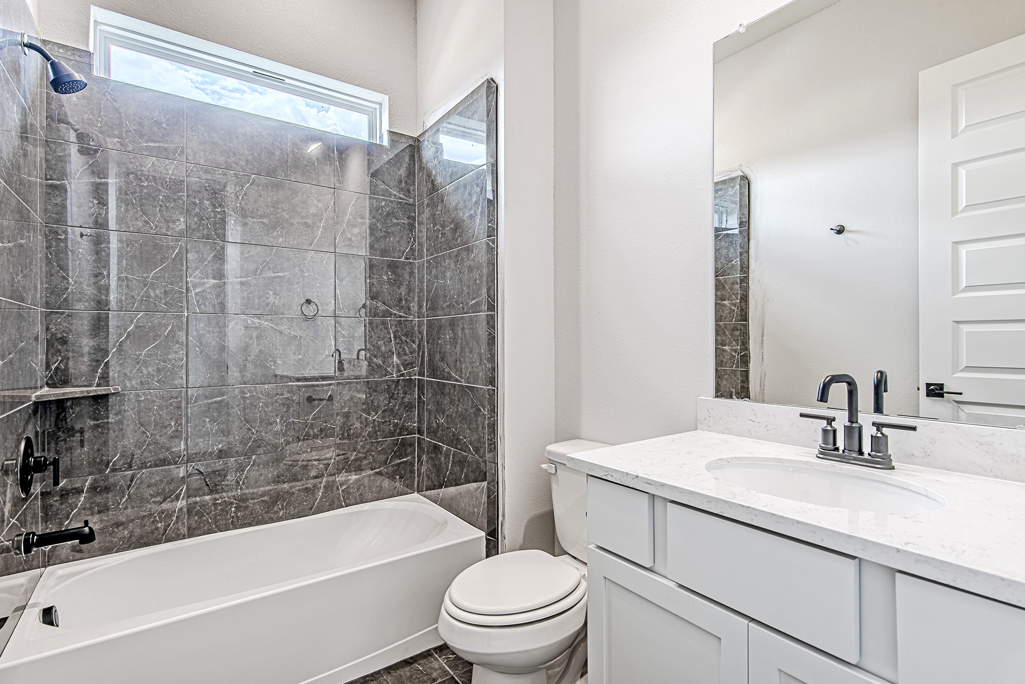 141 Peninsula Point Drive Montgomery, TX 77356 - Photo 29 of 47 A secondary first-floor bathroom featuring elegant gray tile surround, a transom window for soft natural light, and modern matte black fixtures.
