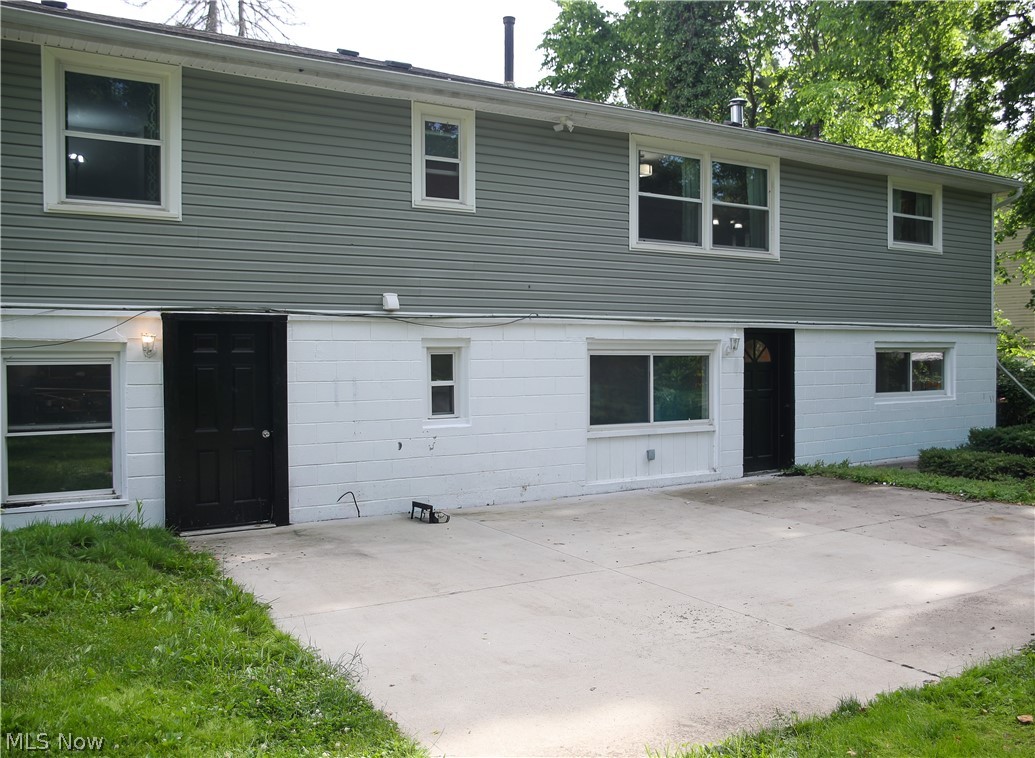 1087 Krumroy Road Akron, OH 44306 - Photo 23 of 23 Lower level exterior featuring a concrete patio, two paneled entry doors, multiple windows, and a combination of white painted brick and horizontal siding