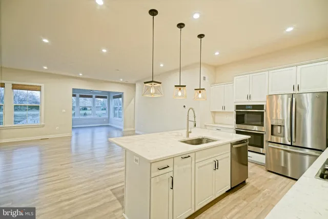 a large kitchen with stainless steel appliances kitchen island granite countertop a stove a sink a refrigerator and white cabinets with wooden floor