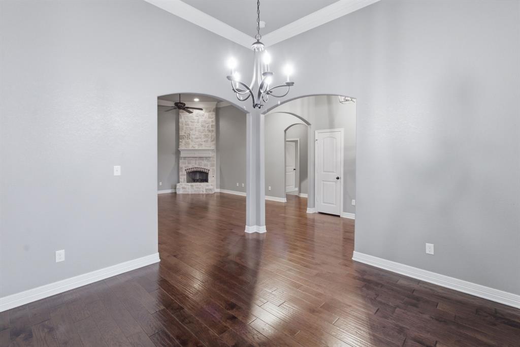 7765 Hickory Spring Lane Tyler, TX 75703 - Photo 9 of 38 Hardwood-finish flooring throughout, featuring a chandelier lighting fixture, arched doorways, and a stone-clad fireplace