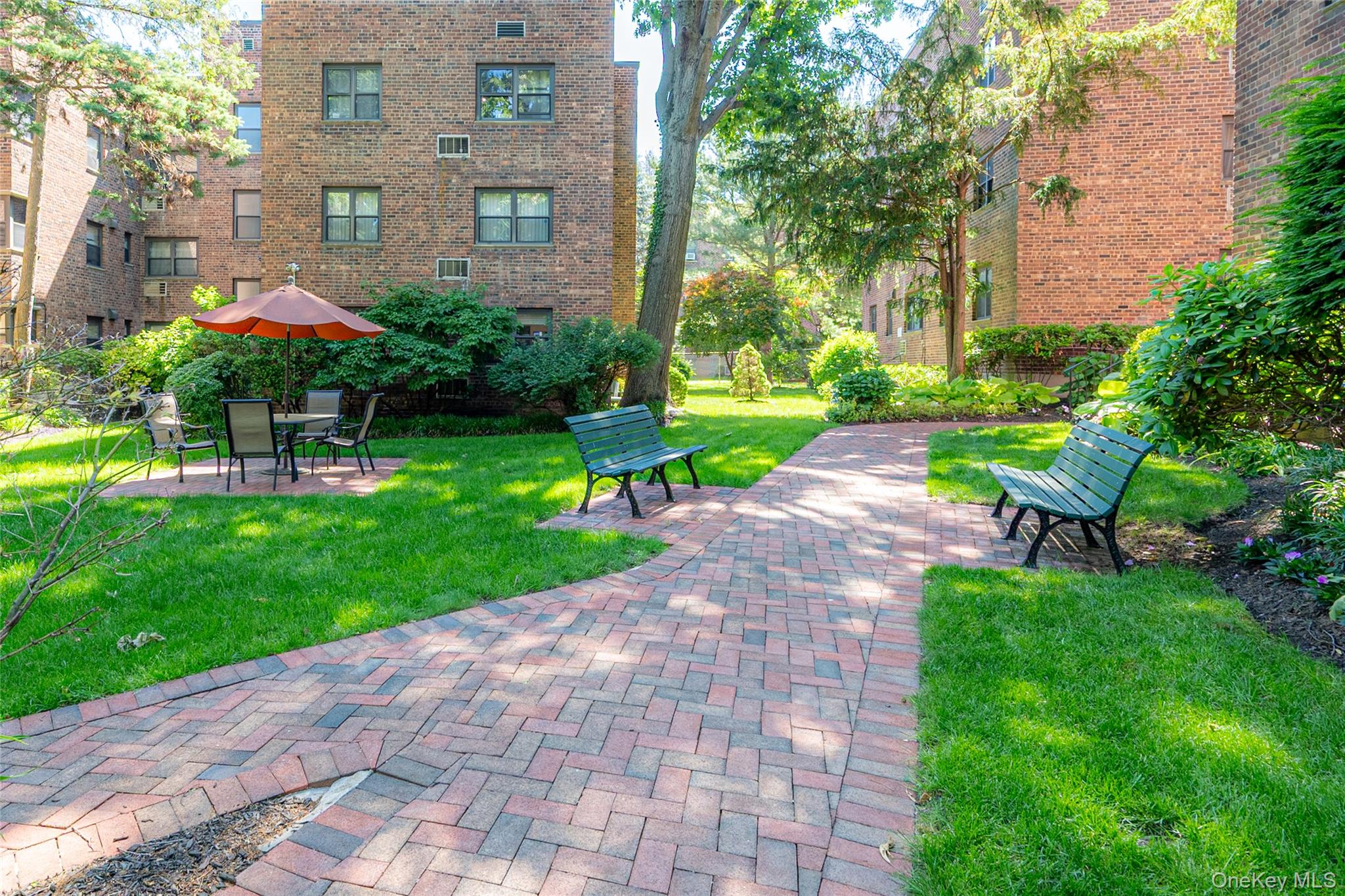50 Brompton Road, Unit 3H Great Neck, NY 11021 - Photo 27 of 28 Landscaped courtyard featuring brick paver pathways, established greenery, and open lawns