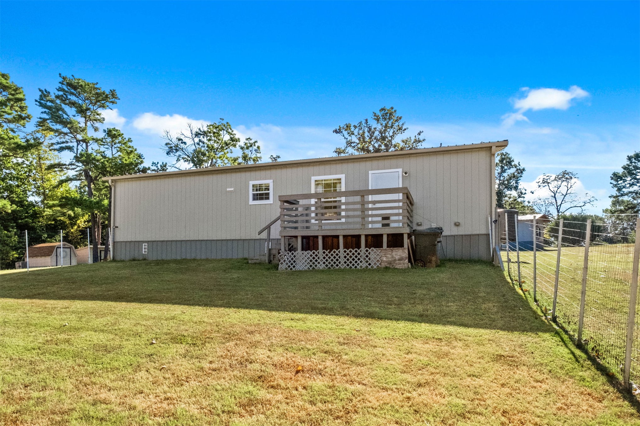 57443 667th Colcord, OK 74338 - Photo 29 of 51 Rear exterior featuring a wooden deck with lattice detailing, a partial chain-link fence, and a detached shed