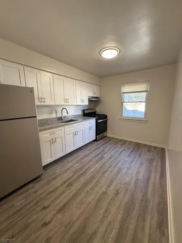 a kitchen with stainless steel appliances granite countertop a refrigerator a sink dishwasher a stove and white countertops with wooden floor