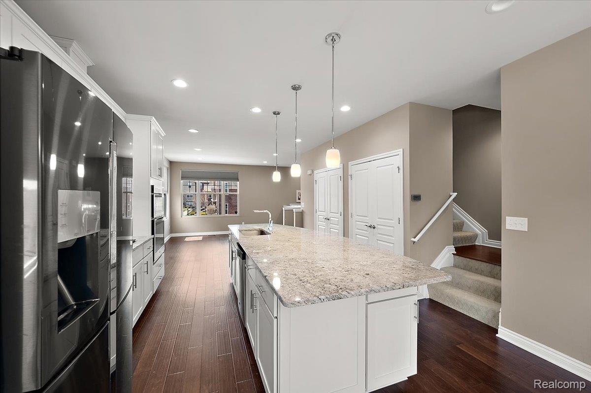 2877 Hartwick Drive Rochester, MI 48307 - Photo 19 of 44 Kitchen with stainless steel appliances, white cabinets, decorative light fixtures, dark wood finished floors, and light stone countertops