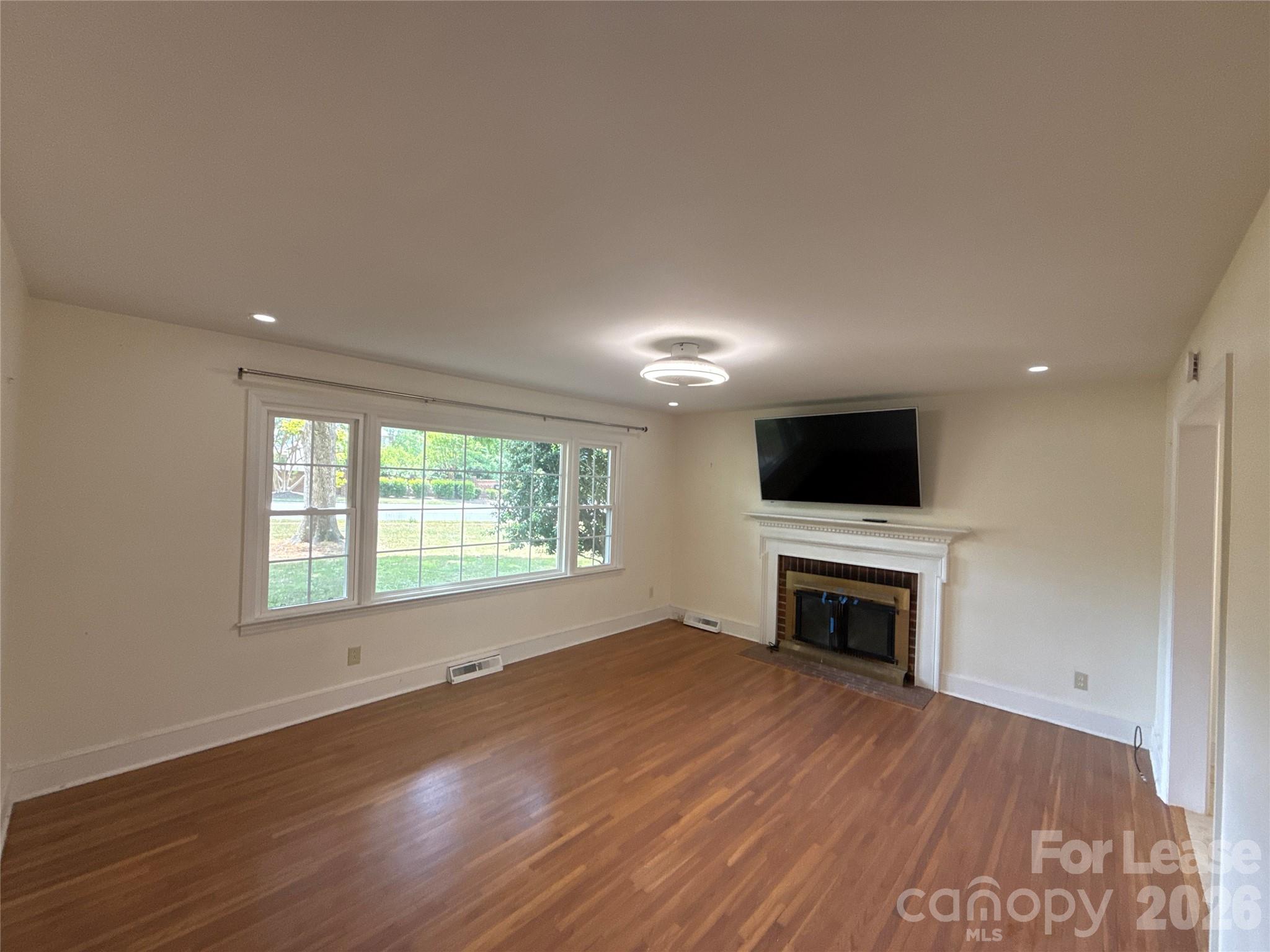 3927 Sharon View Road Charlotte, NC 28226 - Photo 2 of 14 an empty room with wooden floor a flat screen tv a fireplace and a window