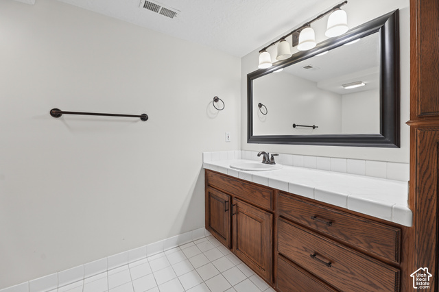 10664 Trail Ridge Circle Sandy, UT 84092 - Photo 56 of 113 Built-in wood-finish vanity with an integrated sink, white tiled countertop, dark bronze fixtures, and a large framed mirror with overhead lighting