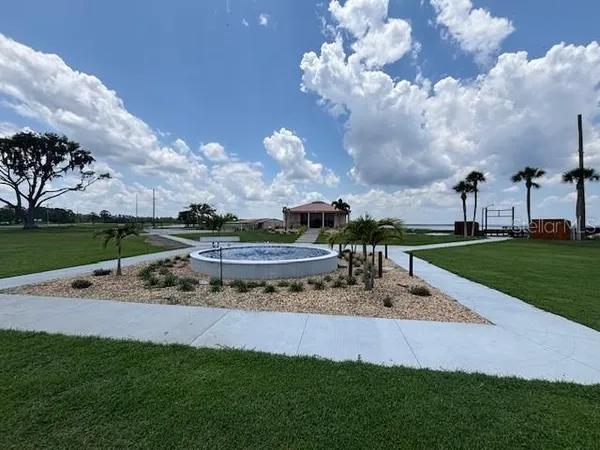 a view of a fountain in front of a big yard with plants and large trees