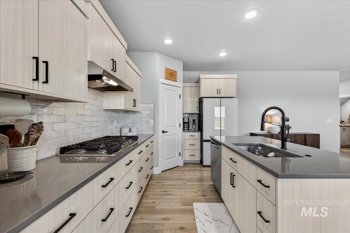 6025 South Catria Place Meridian, ID 83642 - Photo 10 of 34 Kitchen with a center island with sink, light wood-style flooring, recessed lighting, dark stone counters, and stainless steel appliances