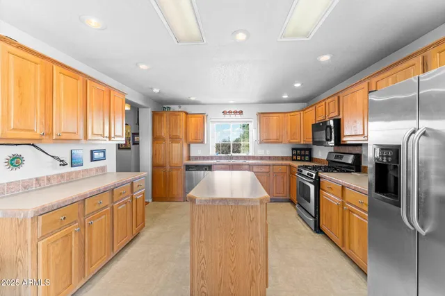 a large kitchen with stainless steel appliances kitchen island granite countertop a large kitchen island a stove a sink a refrigerator and blue cabinets with wooden floor