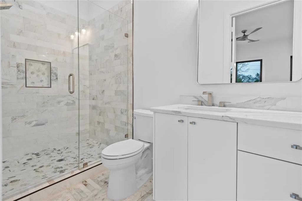 309 Kaye Street Coppell, TX 75019 - Photo 33 of 36 Bathroom featuring a glass-enclosed shower with tiled walls and floor, a white vanity with a countertop, a rectangular mirror, and a modern toilet