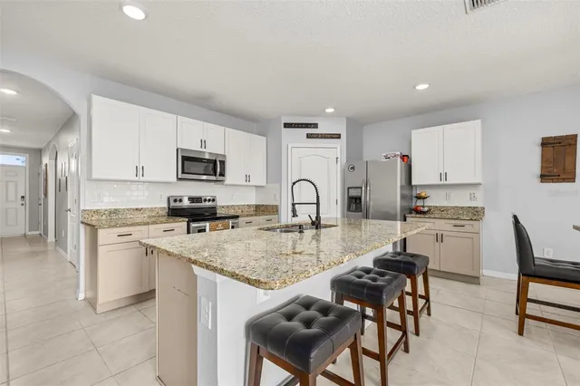 a kitchen with stainless steel appliances granite countertop a stove top oven a sink a refrigerator and white cabinets