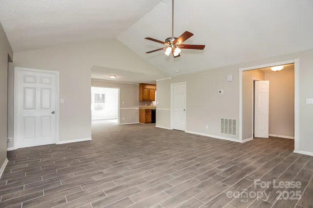 a view of an empty room with wooden floor and a ceiling fan