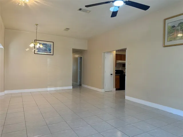 an empty room with kitchen view and a chandelier fan