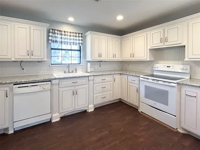 a kitchen with white cabinets appliances a sink and a window