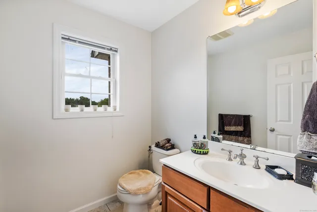 a bathroom with a toilet a sink a mirror and a window