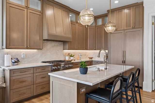 12308 Mariah Circle Draper, UT 84020 - Photo 185 of 293 Guest House Kitchen featuring custom light wood-finish cabinetry, integrated paneled refrigeration, stainless steel professional-grade range, full-height stone backsplash, and a central island with undermount sink