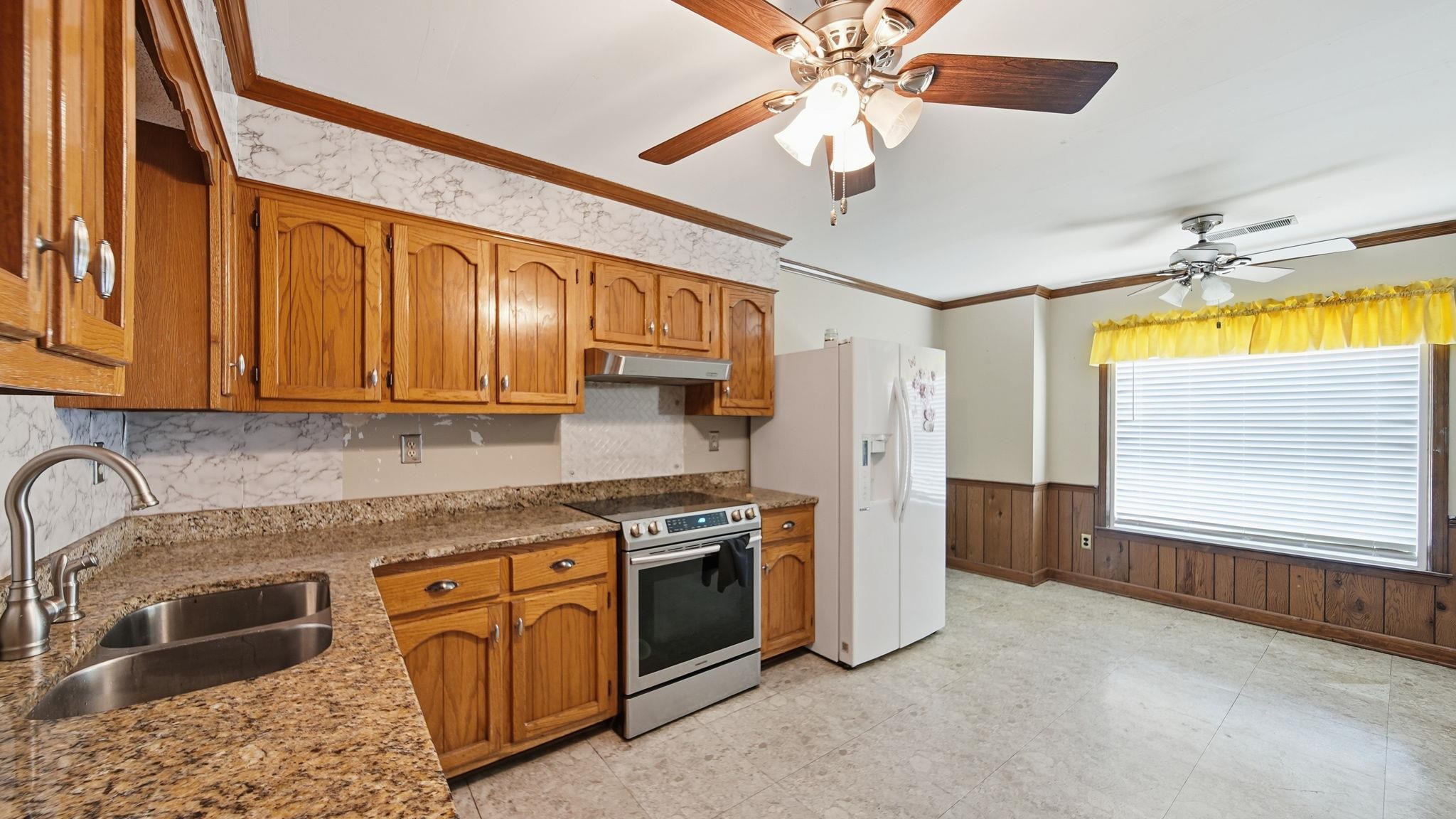 5069 Ross Road Memphis, TN 38141 - Photo 24 of 40 Kitchen with electric range, brown cabinets, crown molding, white refrigerator with ice dispenser, and wainscoting