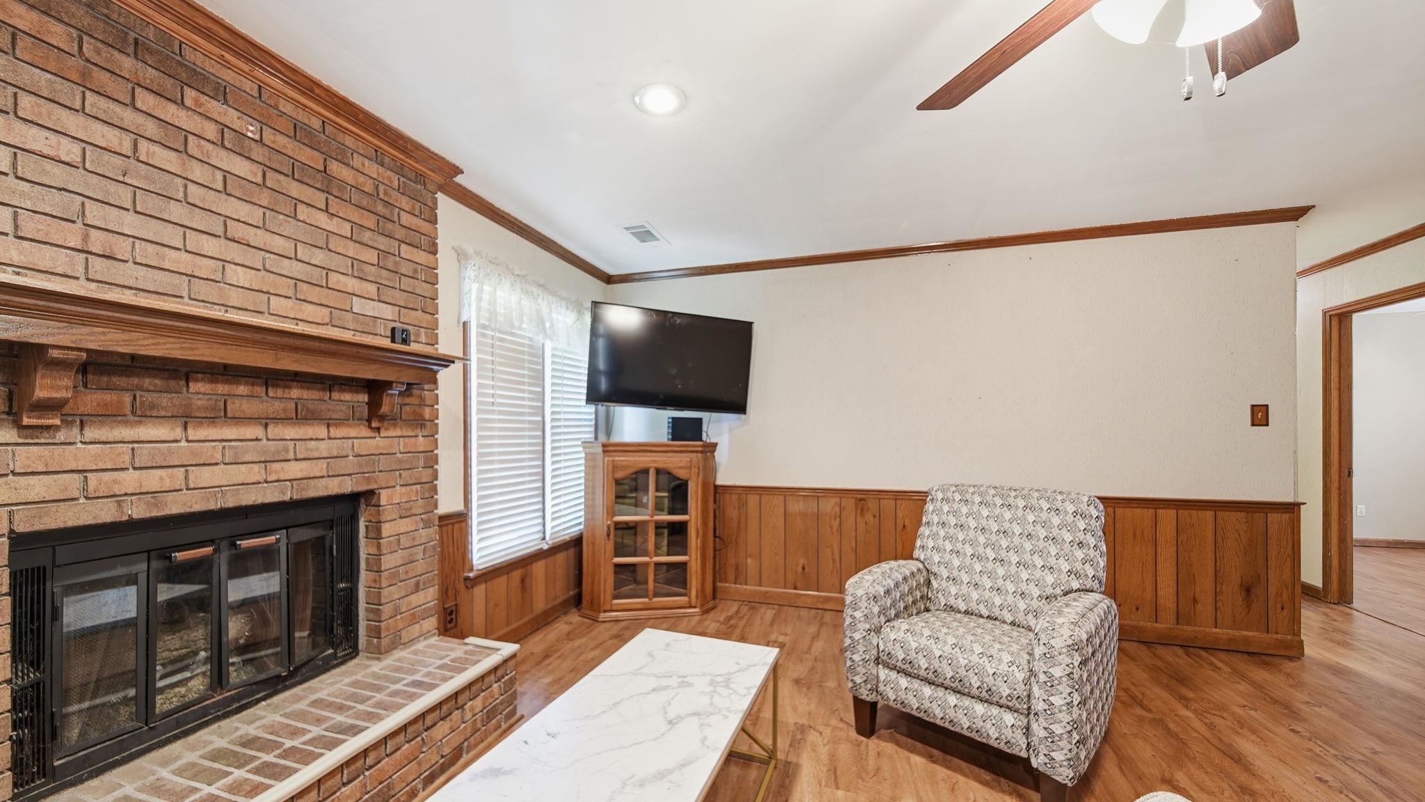 5069 Ross Road Memphis, TN 38141 - Photo 8 of 40 Living room featuring a wainscoted wall, wooden walls, light wood-style floors, ornamental molding, and a brick fireplace