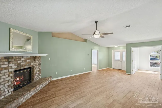 a view of an empty room with wooden floor fireplace and a window